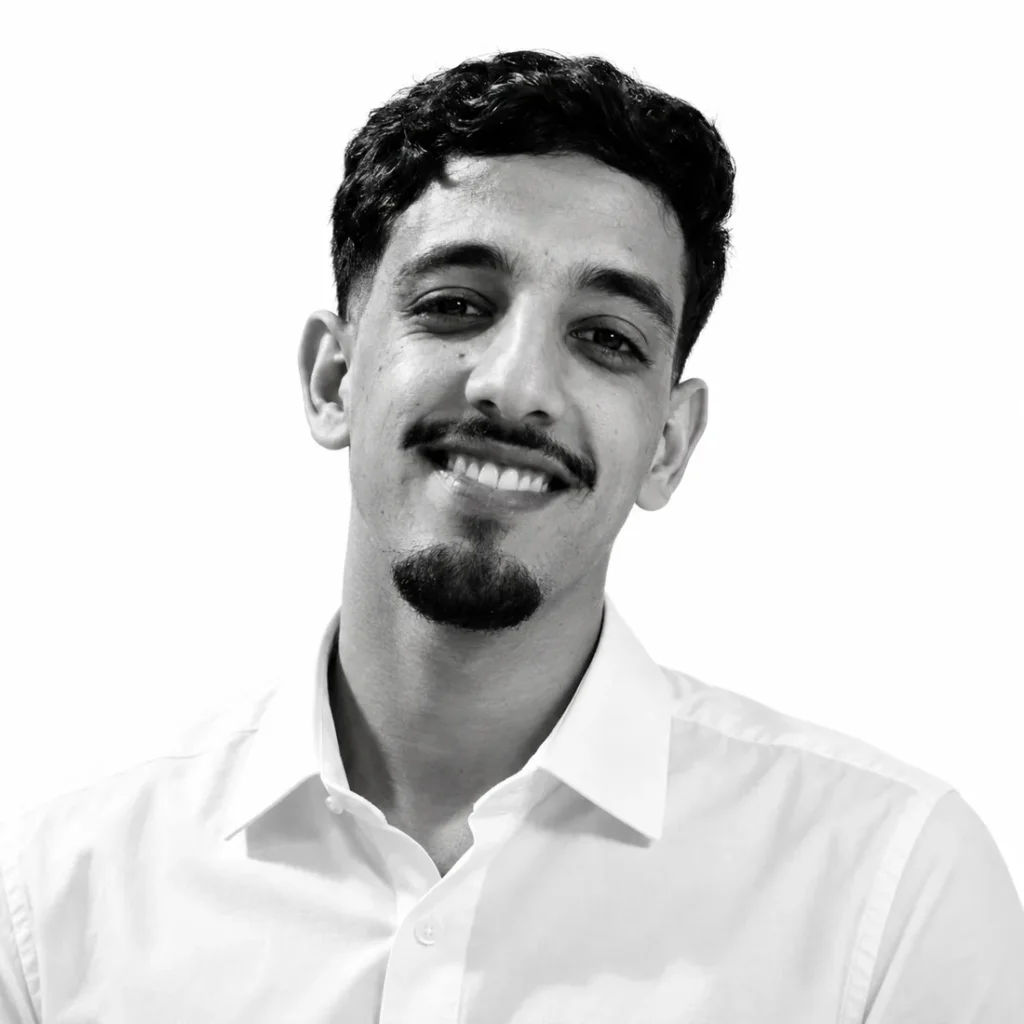Black and white portrait of Hicham AITJAK smiling, wearing a white shirt